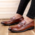 Brown leather loafers worn with black pants on a wooden floor.