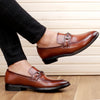 Brown leather loafers worn with black pants on a wooden floor.