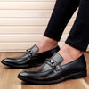 Black dress shoes worn with black pants on a wooden floor.