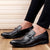 Black dress shoes worn with black pants on a wooden floor.